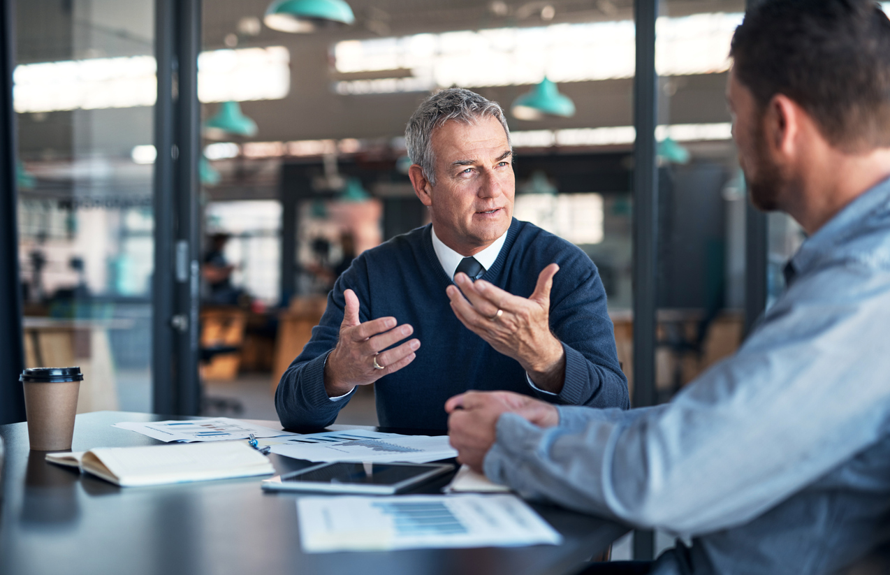 2 men talk over documents on a desk