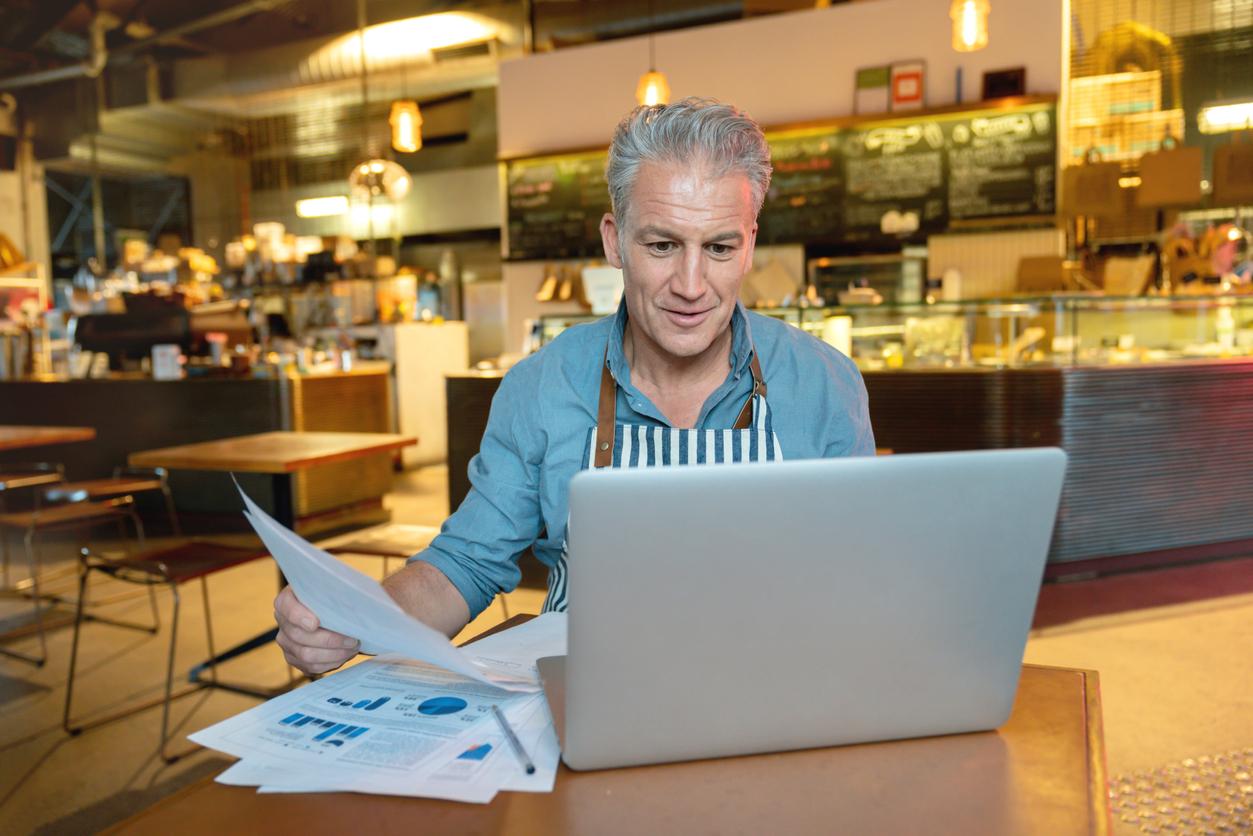 Mature man looks at laptop and papers