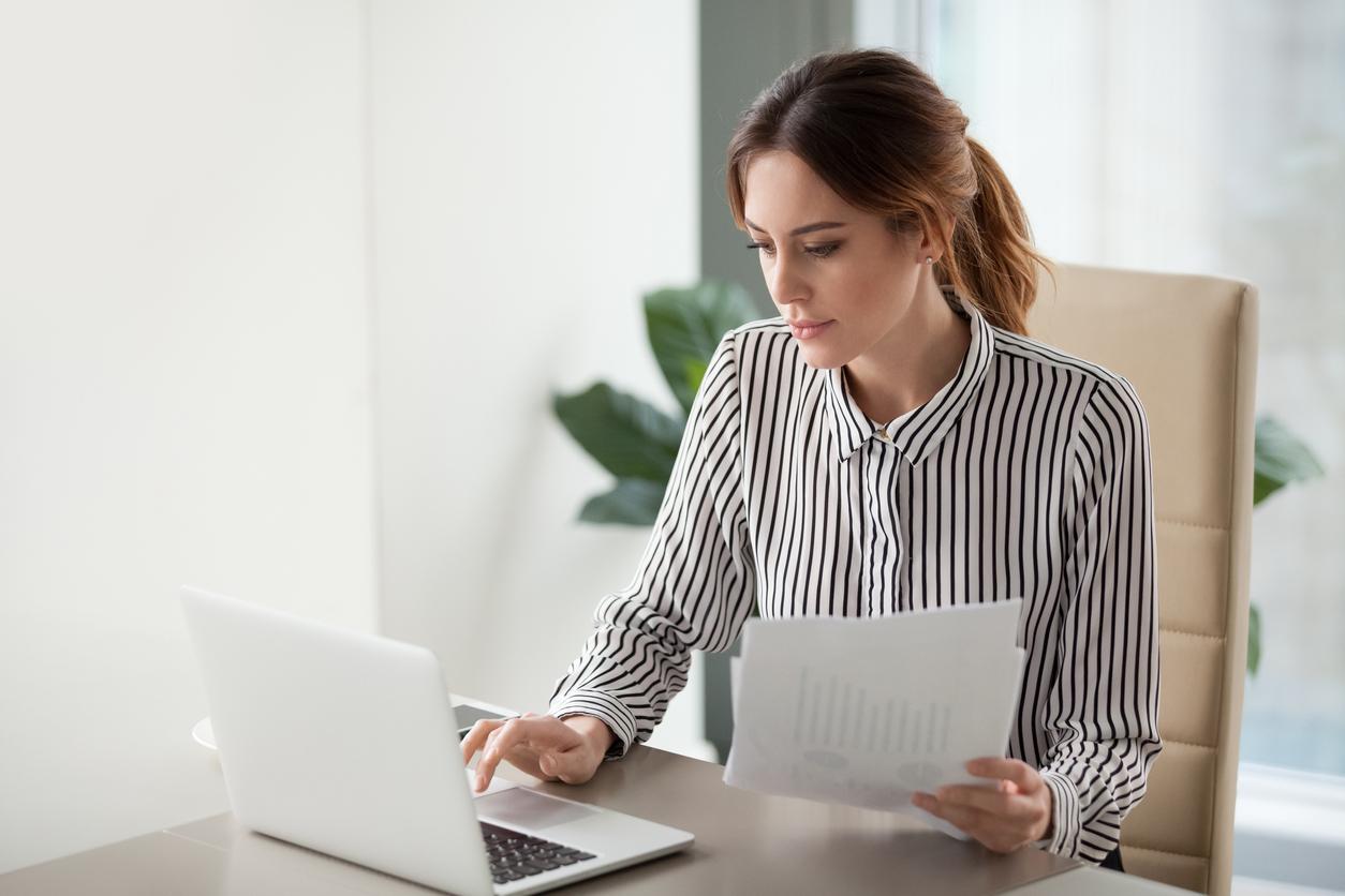 Serious focused businesswoman typing on laptop holding papers