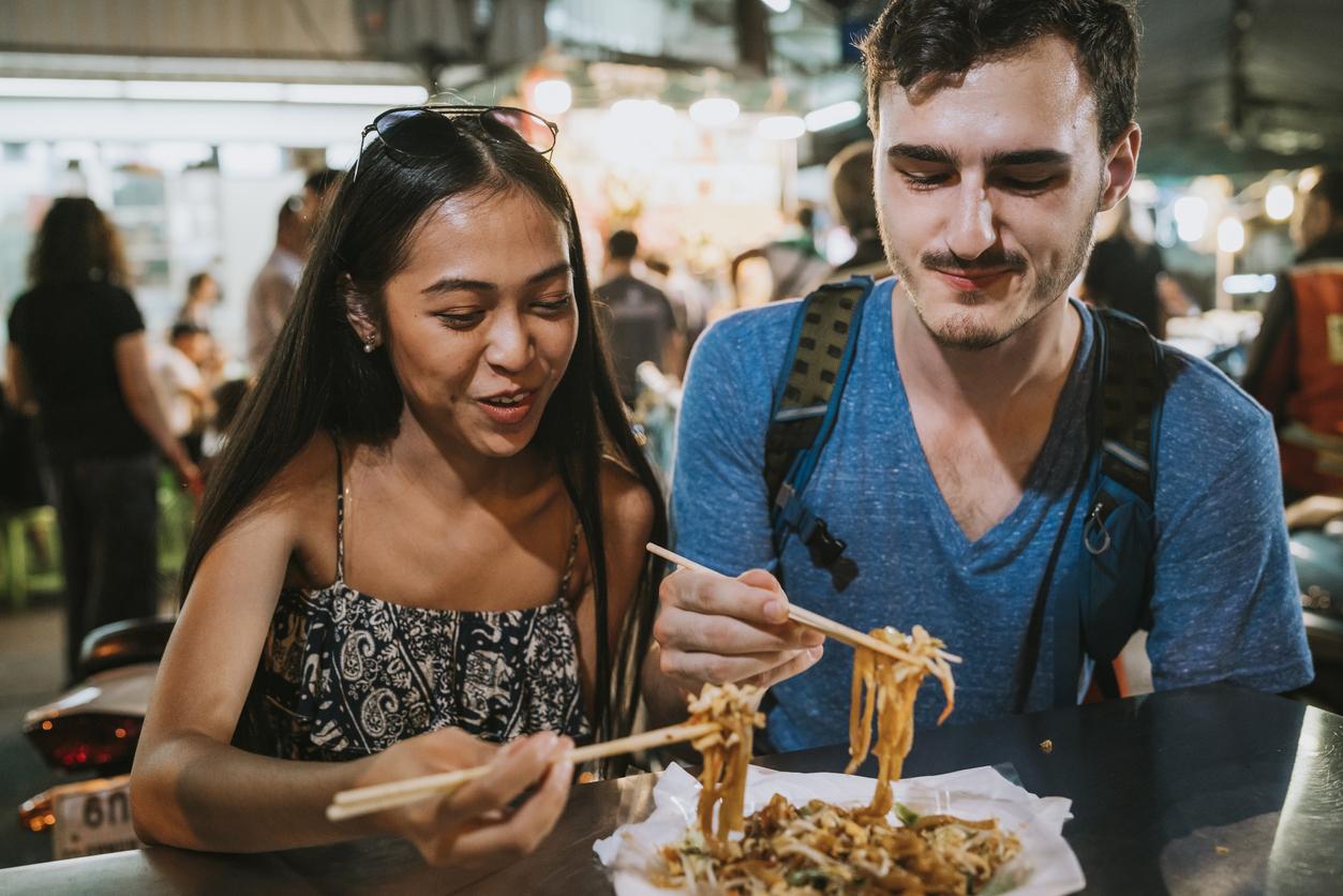 Man and woman eat noodles outdoors