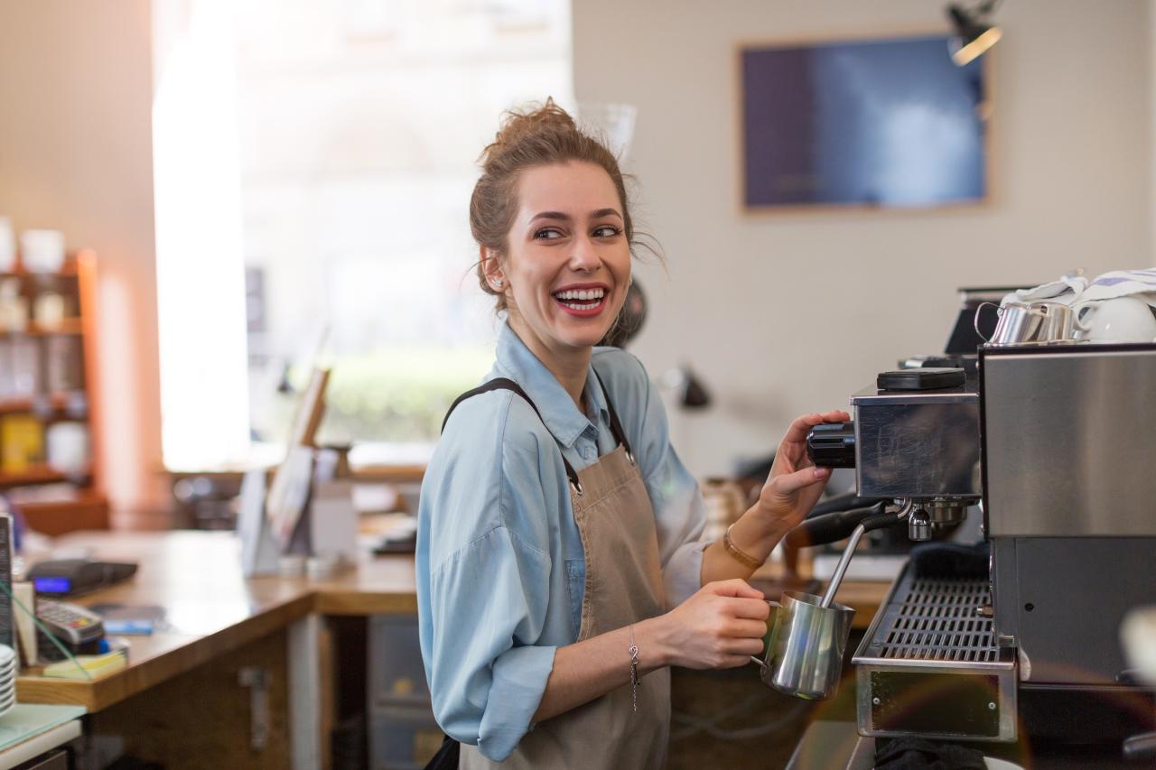 Young barista preparing coffee for customers at her cafe counter