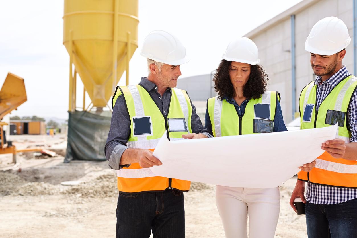 Woman and two men read plans on construction site