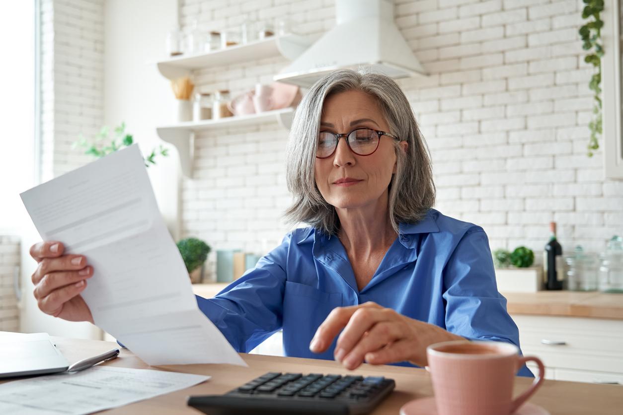 Senior mature business woman holding paper bill using calculator