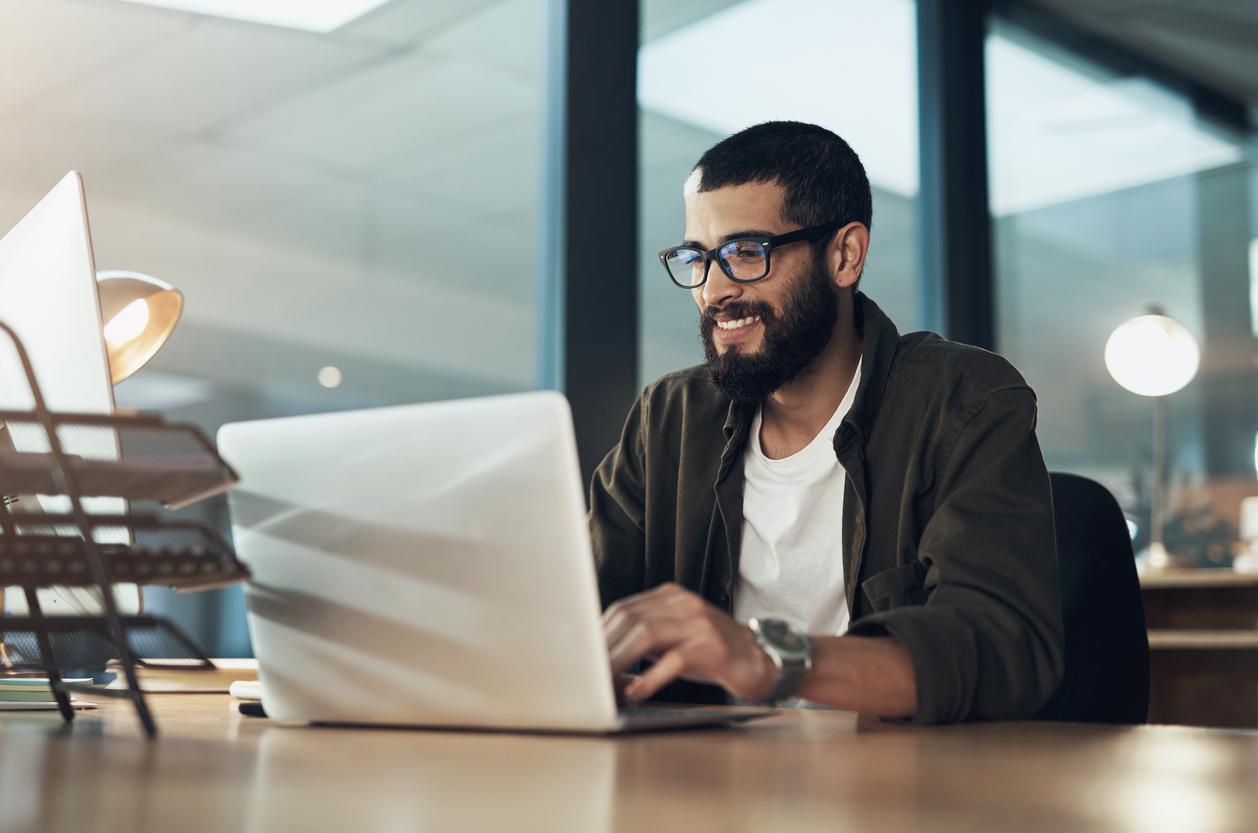 Bearded man with glasses smiles at laptop