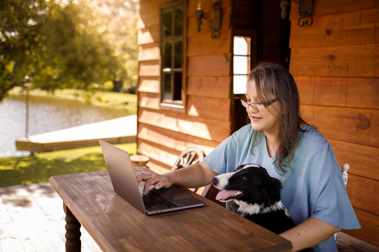 Woman with dog looks at laptop in countryside