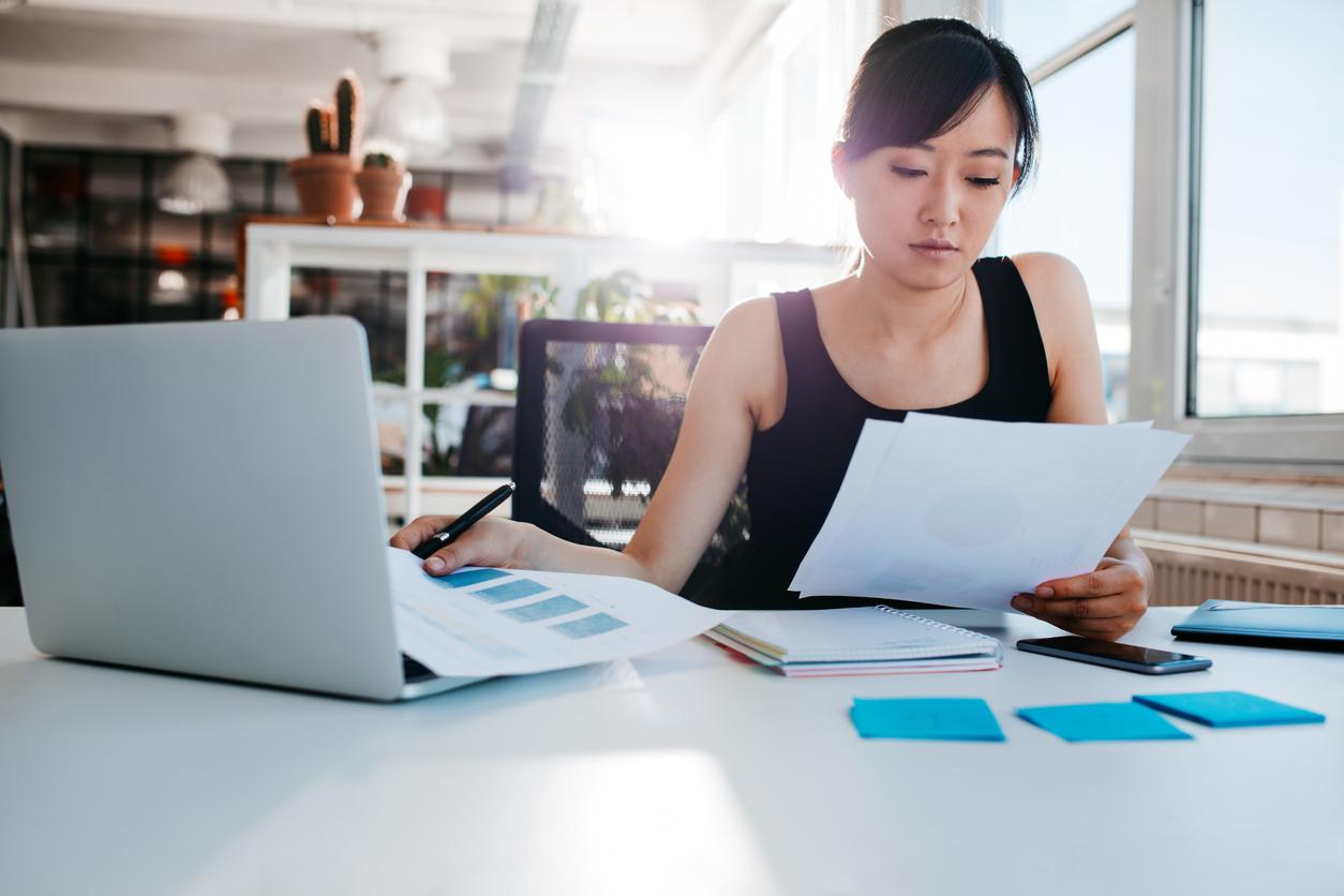 Woman sits at table with laptop and paperwork