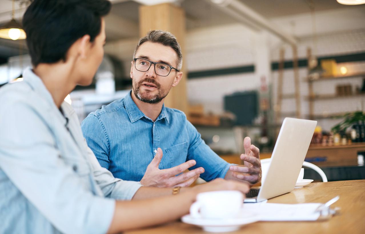 Man and woman talk at table with laptop and papers