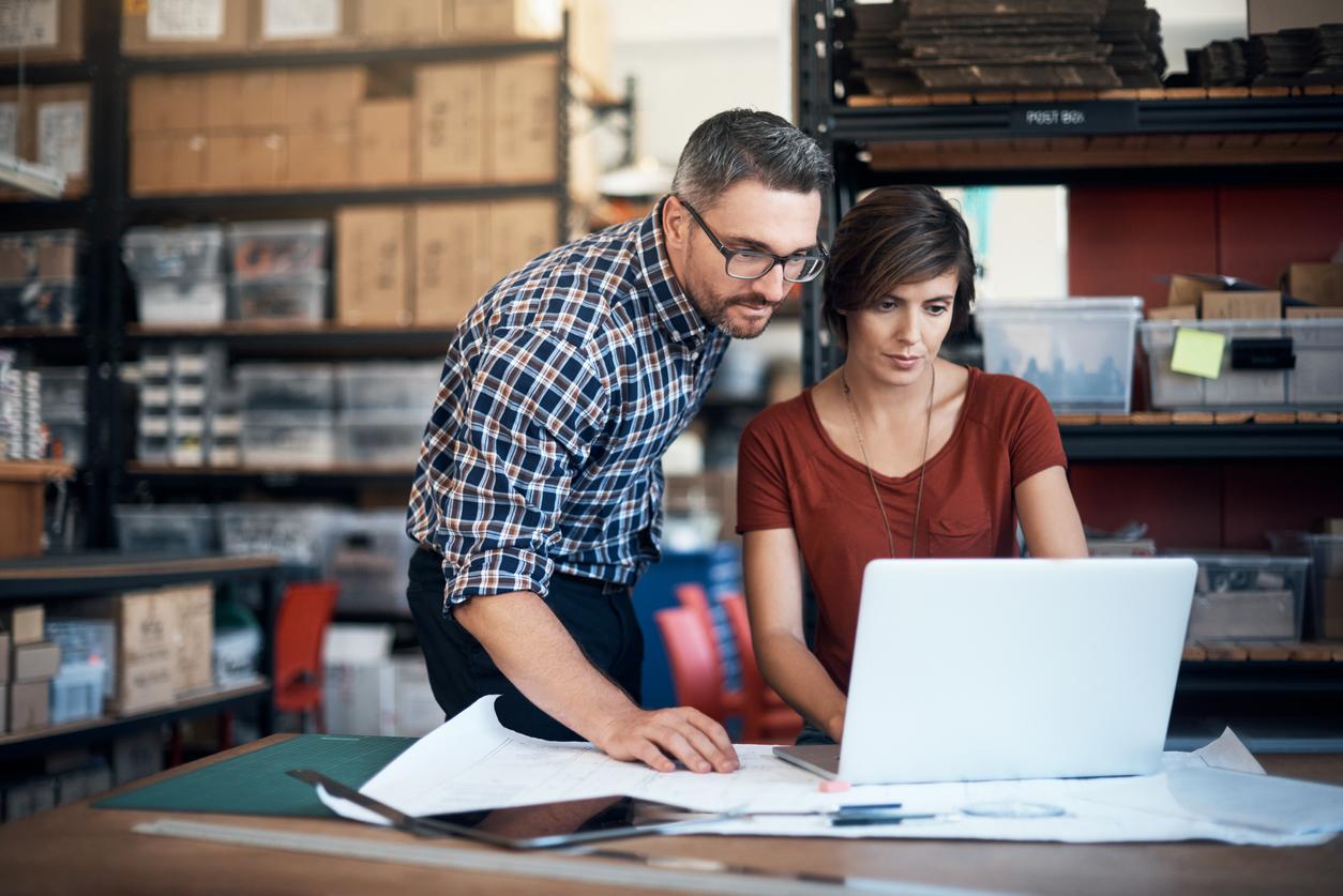 Man and woman using a laptop while working on a project together in a workshop