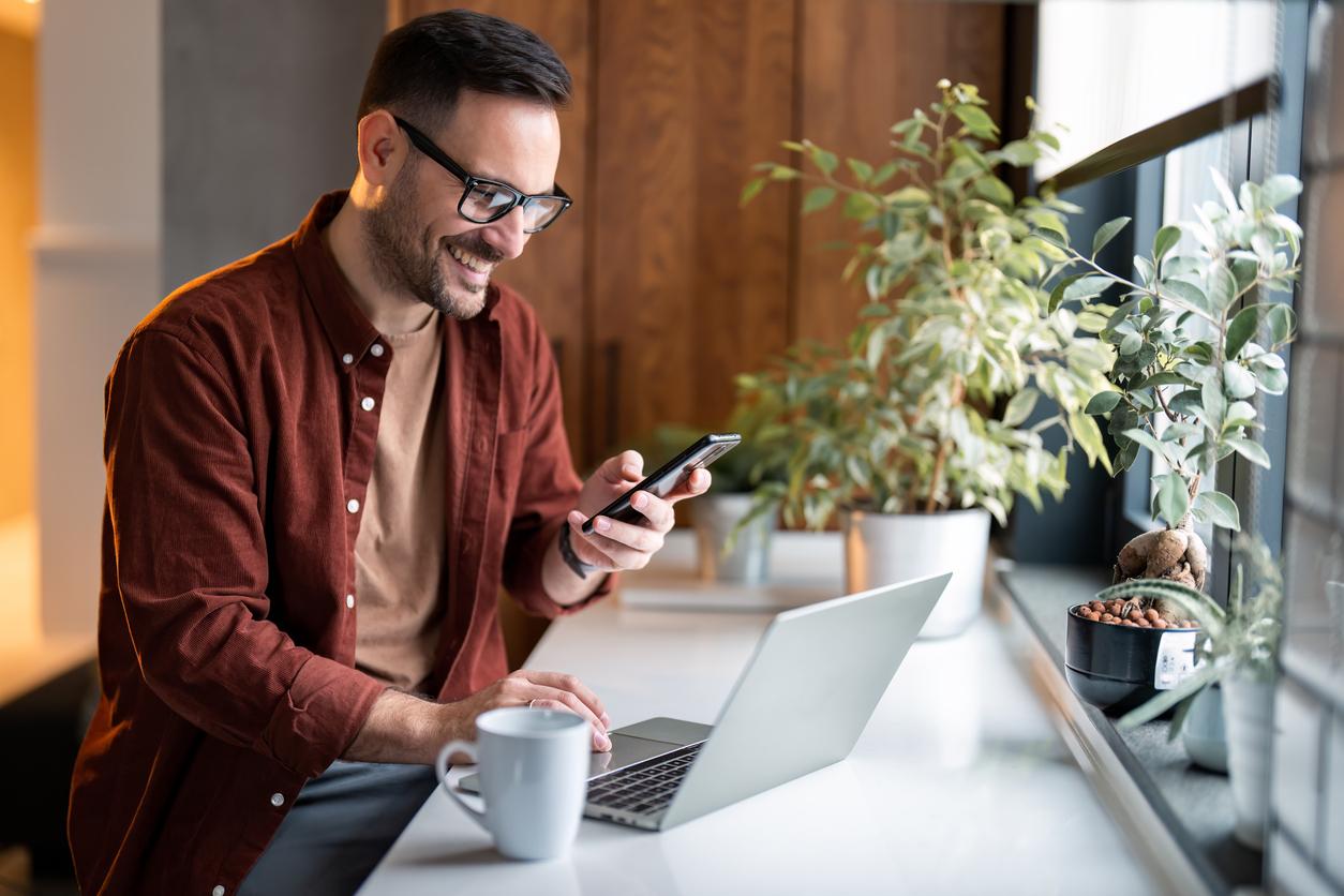 Satisfied modern millennial man in stylish casual clothes using smartphone and laptop